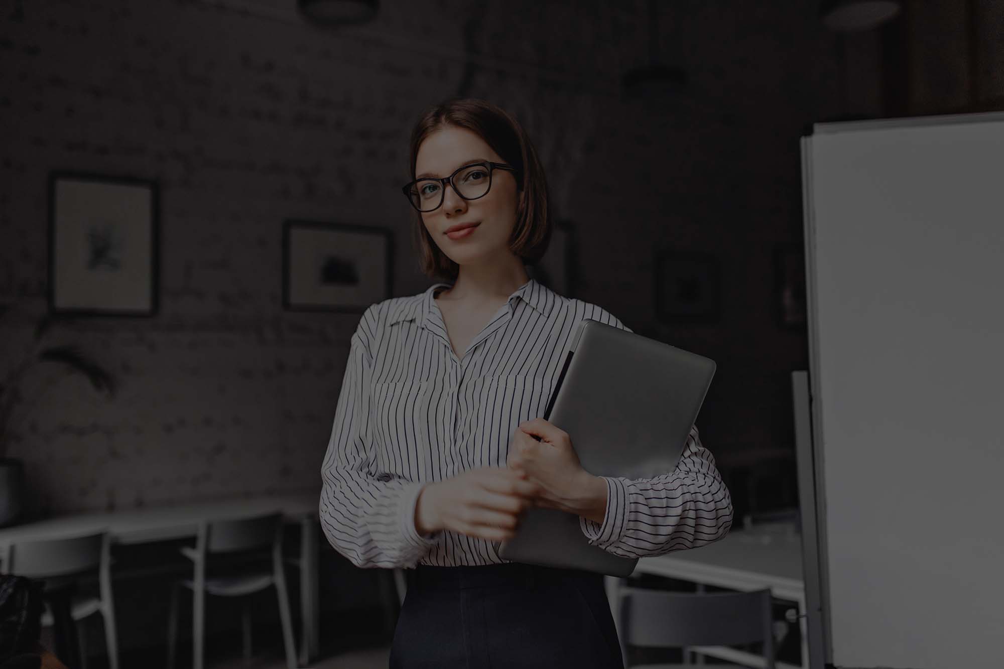 portrait of brown eyed business woman in black and white outfit and stylish glasses posing with laptop in white room low overlay