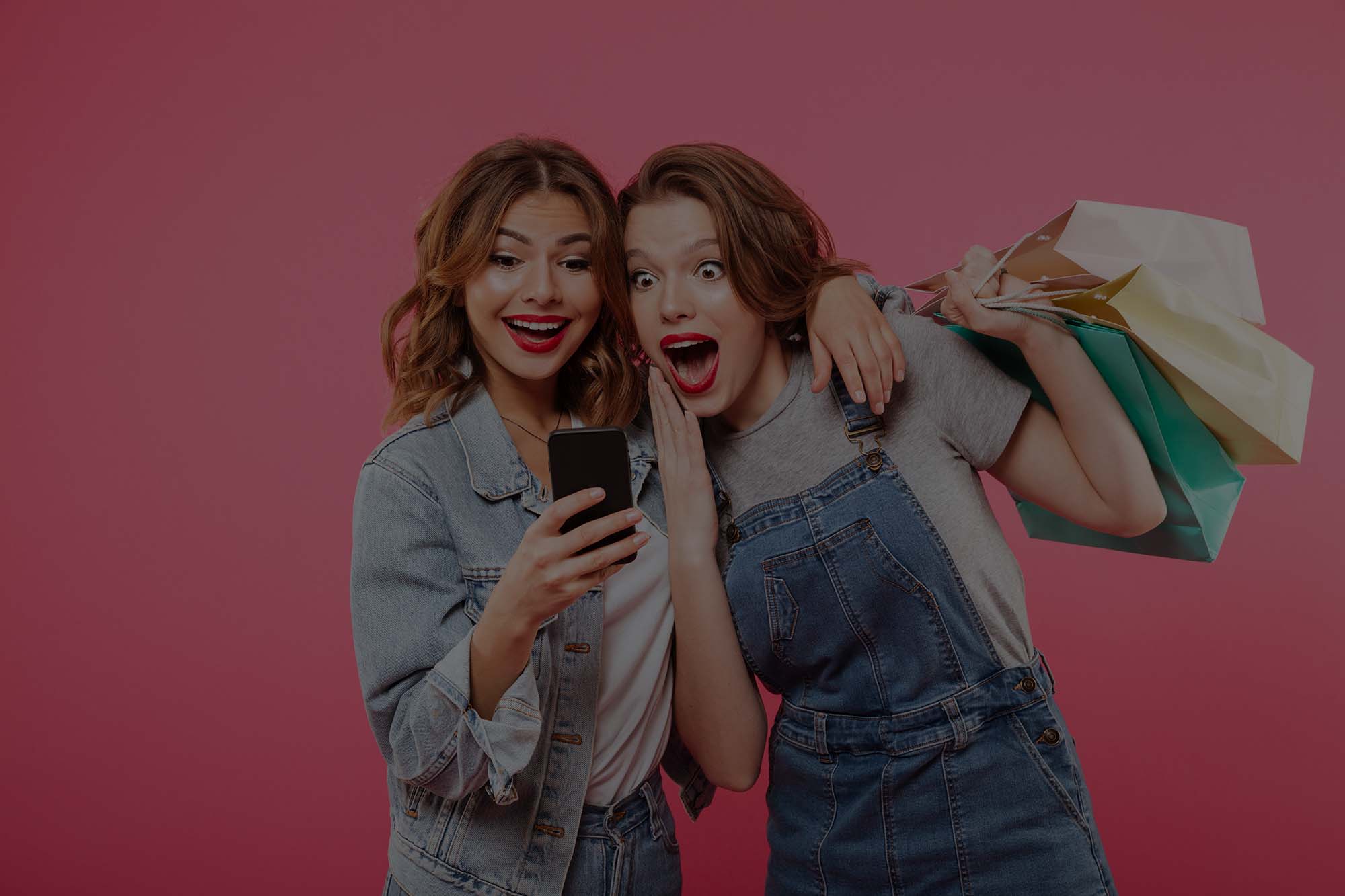 shocked two women friends holding shopping bags using mobile phone low overlay