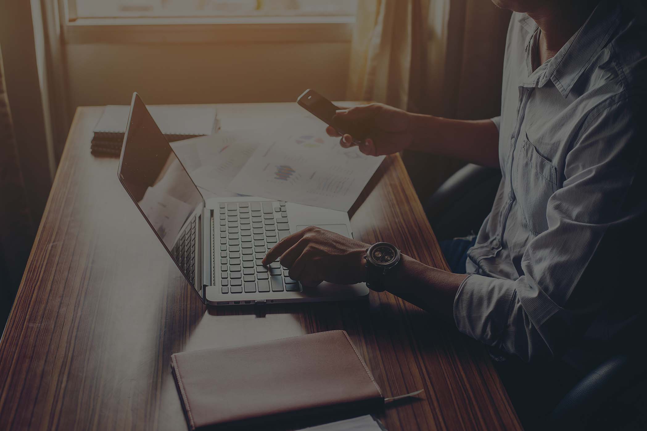 businessman hands using cell phone with laptop at office desk low overlay