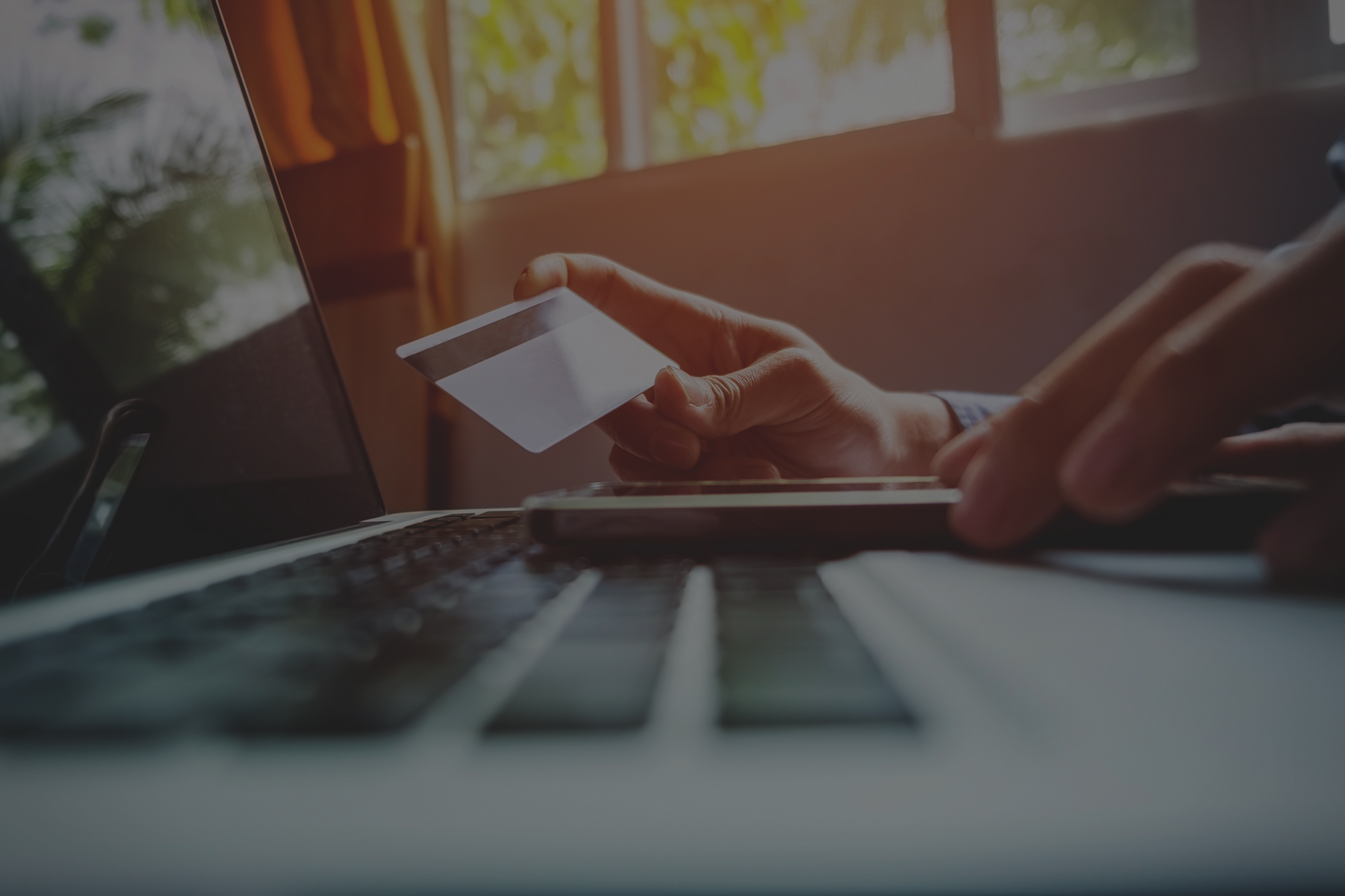 man holding credit card in hand and entering security code using smart phone on laptop keyboard online shopping concept low overlay