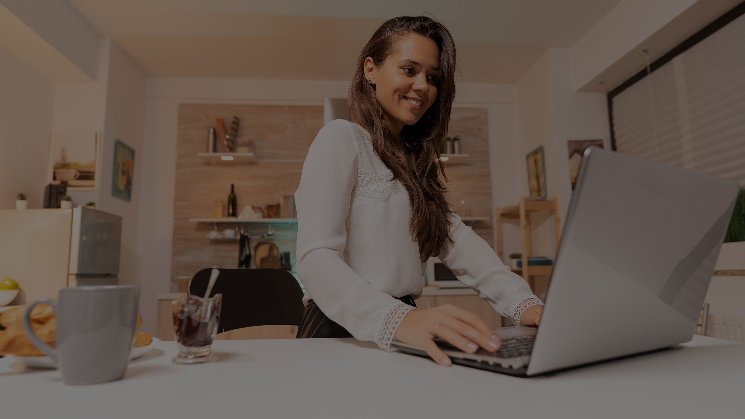 woman working on her small business using laptop in home at night concentrated smiling entrepreneur in home kitchen using notebook during late hours in the evening low overlay